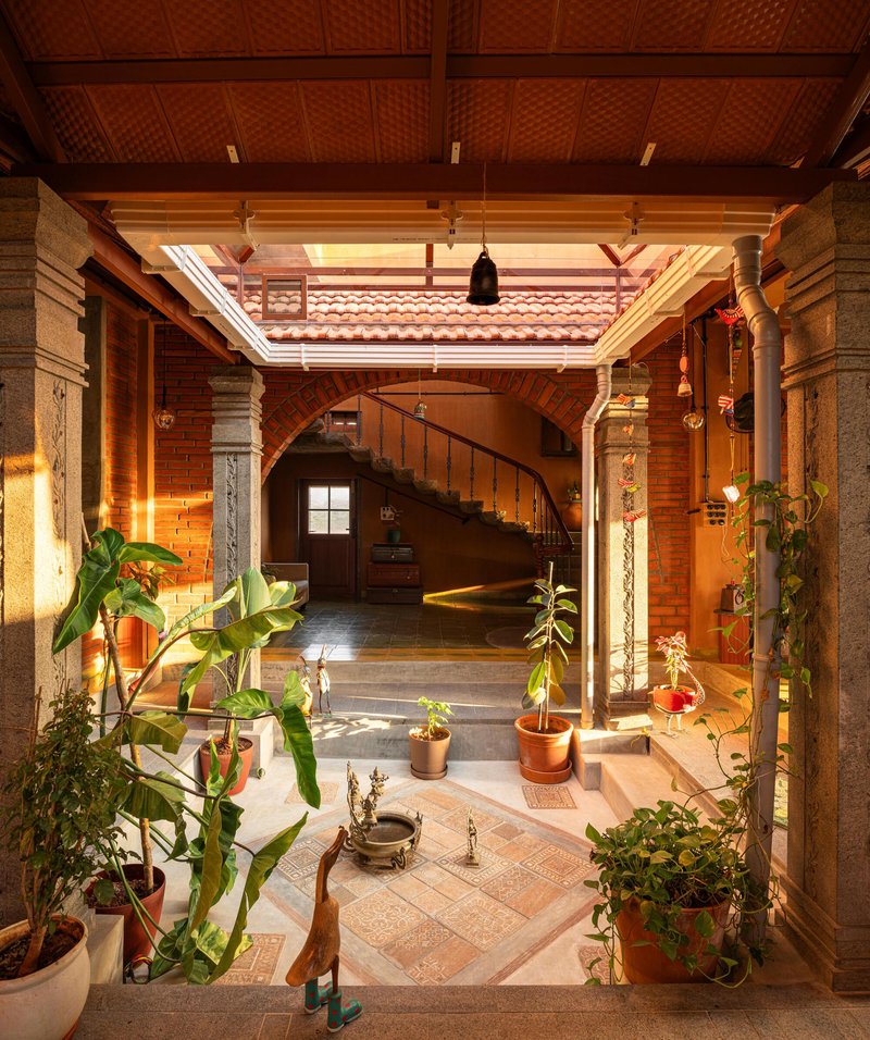 Interior courtyard with potted plants, carved stone columns, curved staircase and woven bamboo ceiling