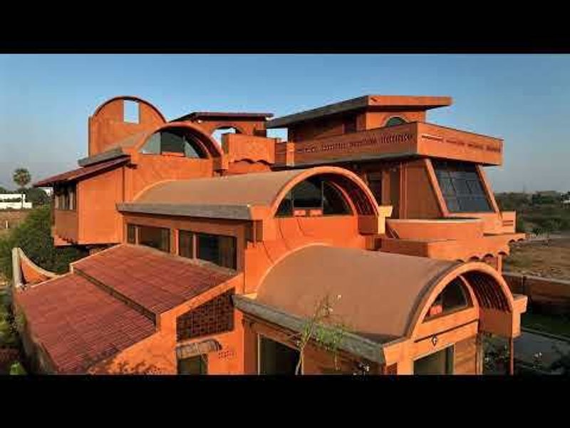 Aerial view of the terracotta-colored residence with barrel vault roofs and staggered terraces under a clear blue sky