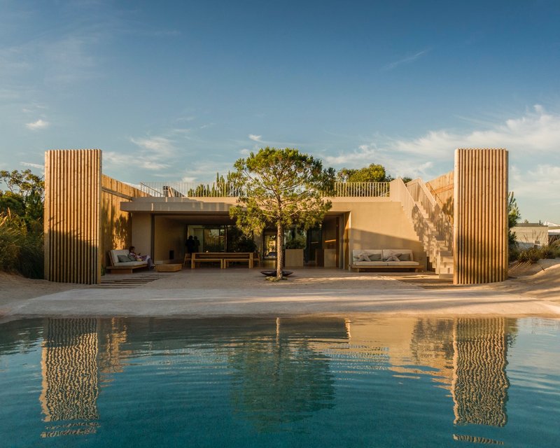 View across the swimming pool toward the timber-slatted facade and terrace in afternoon light