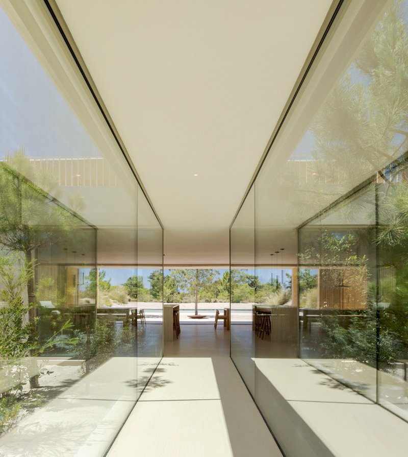 Glass-walled corridor with reflecting polished floor leading to outdoor dunes and grasses