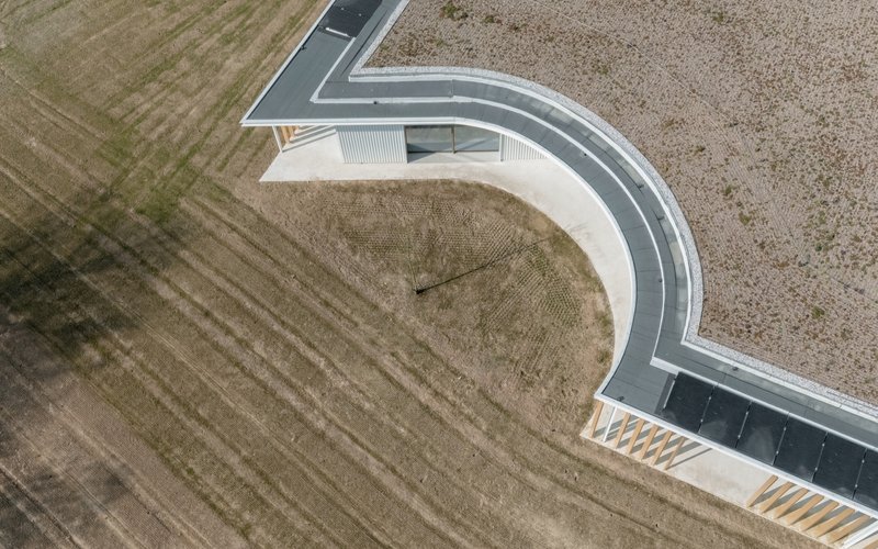 Aerial view of the curved roofline and black asphalt pathway cutting through surrounding agricultural fields
