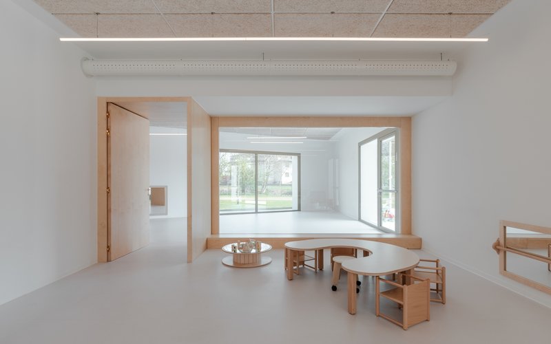 Interior space with timber window seat overlooking the lawn and curved wooden tables on resin flooring