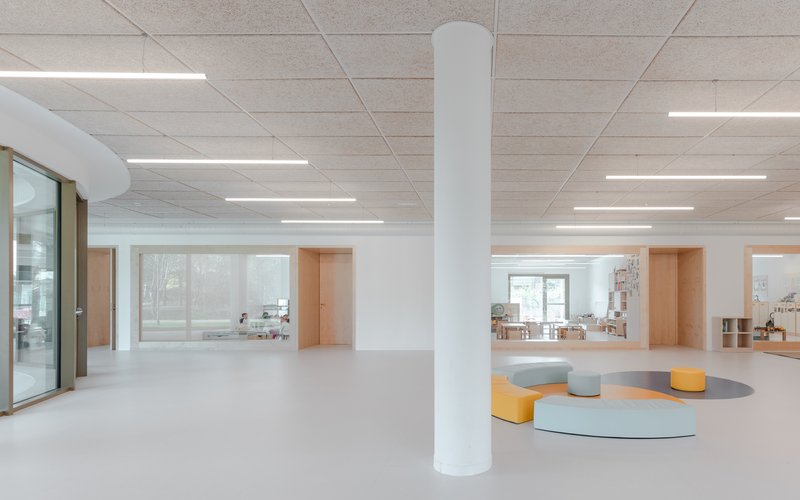 Interior space with white ceiling panels, linear lighting, and circular seating elements on pale flooring