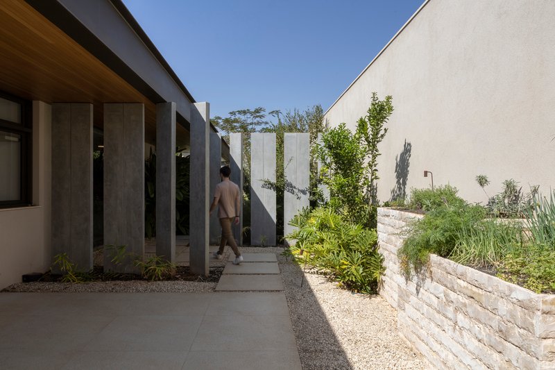 Exterior walkway with vertical metal fins alongside a white stone retaining wall and figure walking