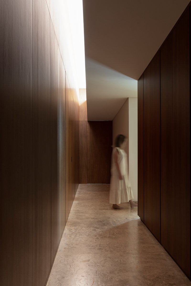 Corridor with floor-to-ceiling timber wall panels and natural light filtering through a clerestory above