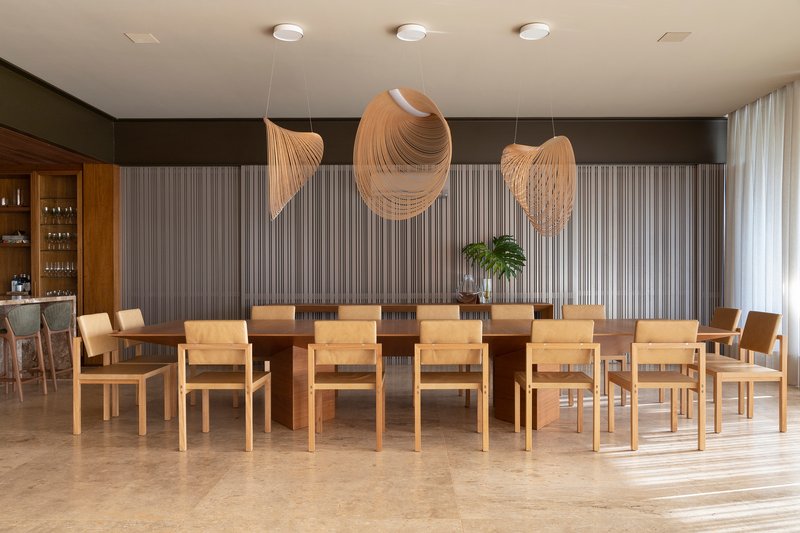 Dining room with long timber table surrounded by light wood chairs beneath sculptural pendant fixtures and vertical paneling