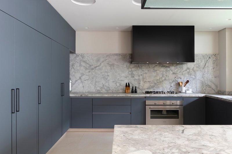 Kitchen with charcoal cabinets and white marble backsplash under recessed ceiling lighting