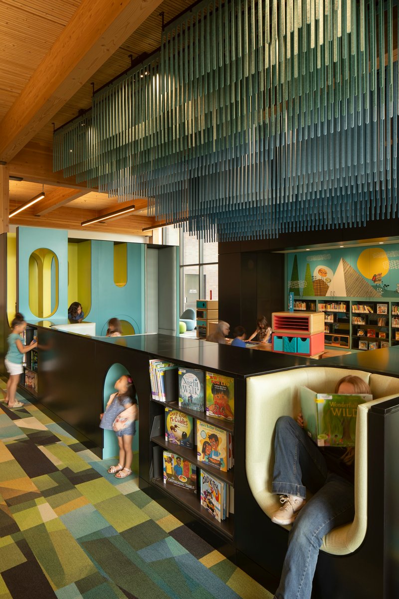 View of curved reading nooks with integrated shelving below suspended glass rod screen and timber beam structure