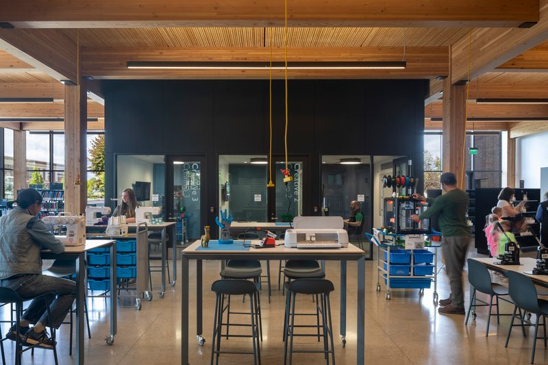 Workshop space with central table, black metal core volume and timber post-and-beam structure under natural light