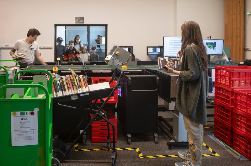 Book sorting workspace with automated conveyor system and colored bins behind a glass partition
