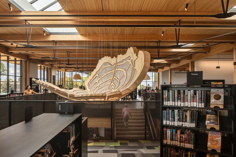 Laminated timber sculpture hanging above the main staircase with exposed wooden ceiling beams and skylights overhead