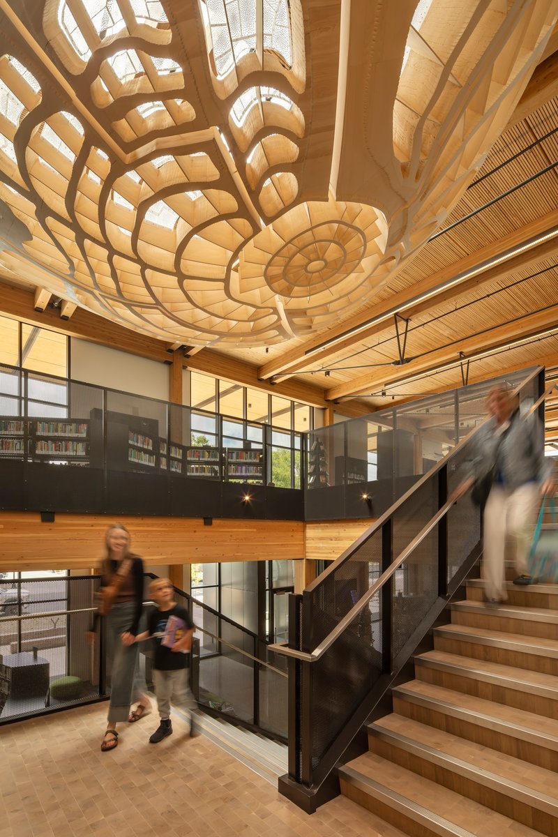 Double-height atrium with sculptural timber ceiling ribs and visitors ascending the wooden staircase
