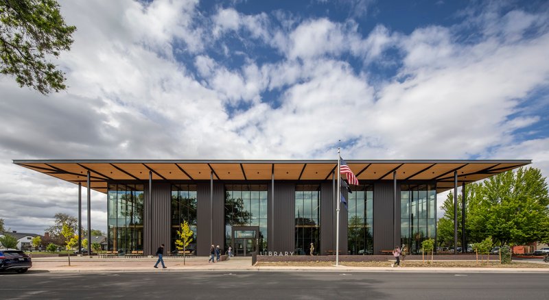 Street view of the glazed facade with dark corrugated metal cladding and wide timber canopy under scattered clouds