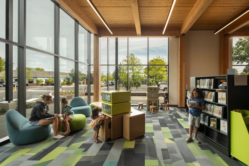 Reading area with patterned carpet tiles and glulam timber ceiling beams beneath tall glazed walls