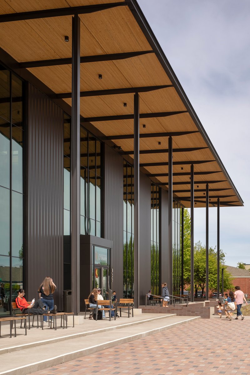 Covered entry plaza with slender steel columns supporting the timber-lined canopy above seated visitors