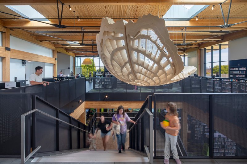 Upper level mezzanine with perforated metal balustrade and suspended sculptural pendant light overlooking patrons on stairs