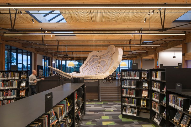 Library interior with suspended timber ceiling installation above dark shelving and patterned floor