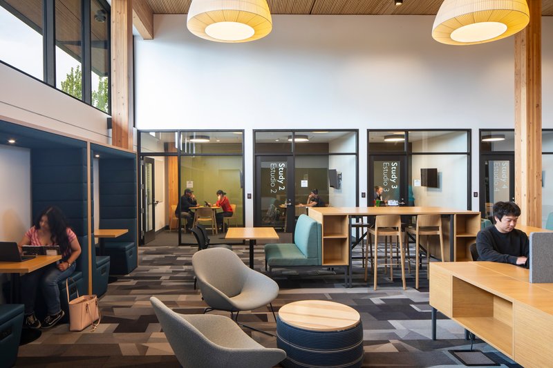 Reading area with glass-walled study rooms and visitors seated at tables under pendant lights