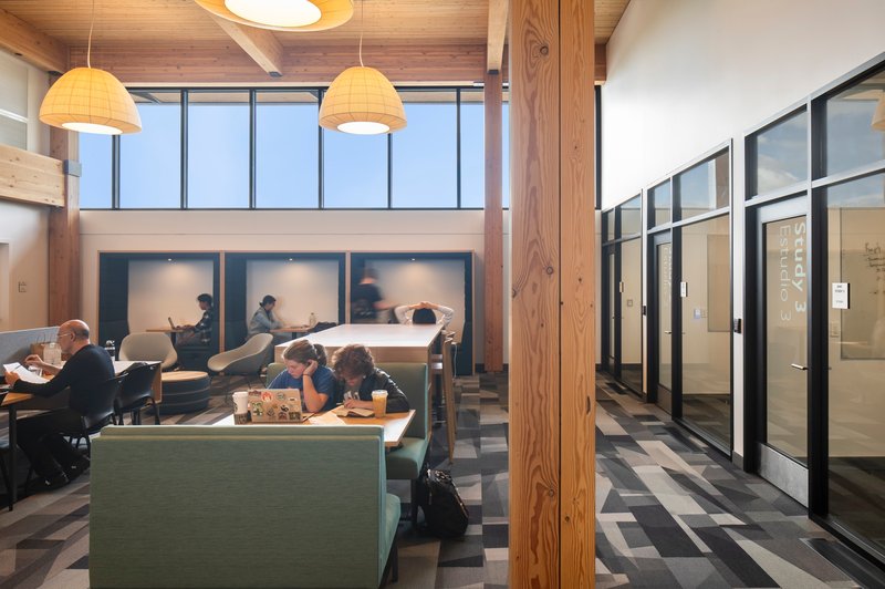 Open study space with timber columns, glass-enclosed meeting rooms, and students at shared tables