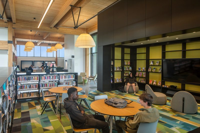 Reading area with round tables and pendant lights under a timber ceiling with two patrons conversing