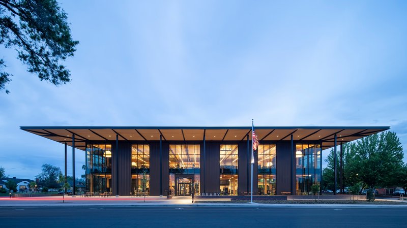 Street view of the glass and steel facade with deep roof overhang at dusk