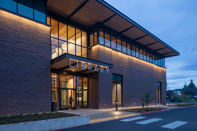 Entry canopy with glazed walls and illuminated brick facade at twilight with figure departing
