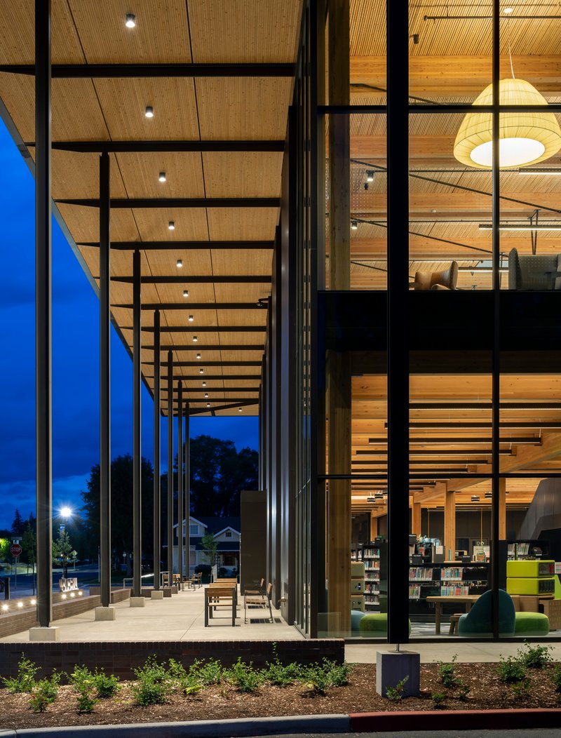 Covered walkway with slender steel columns framing views into the lit interior at blue hour