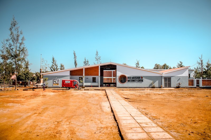 Frontal view showing the gabled roof forms with perforated screens and a concrete pathway across the compound