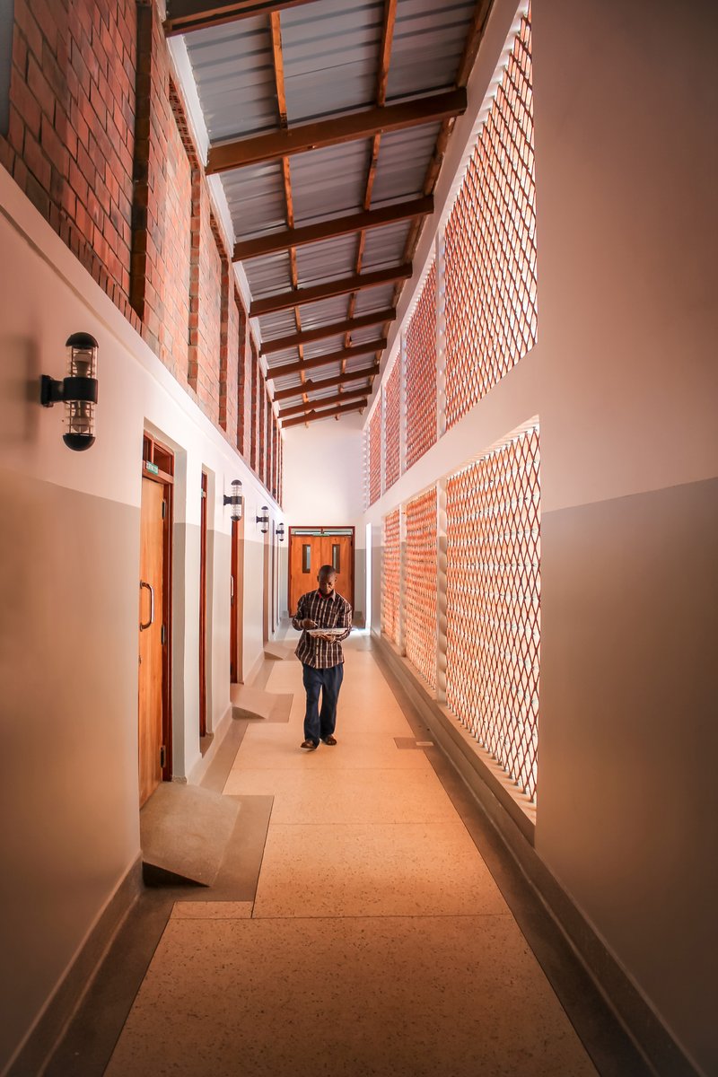 Corridor with perforated brick walls, exposed timber ceiling beams and a person walking through dappled light