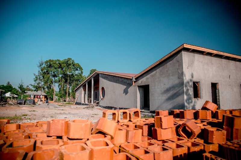 Ground-level view showing scattered orange bricks in foreground and linked pavilions with exposed structure beyond