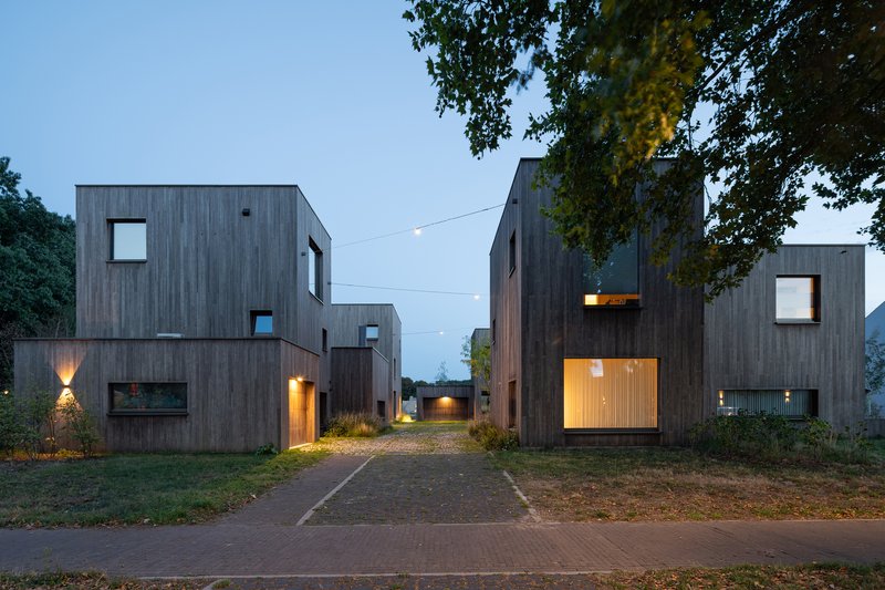 Entry lane at dusk with illuminated windows and doorways in the timber-clad volumes