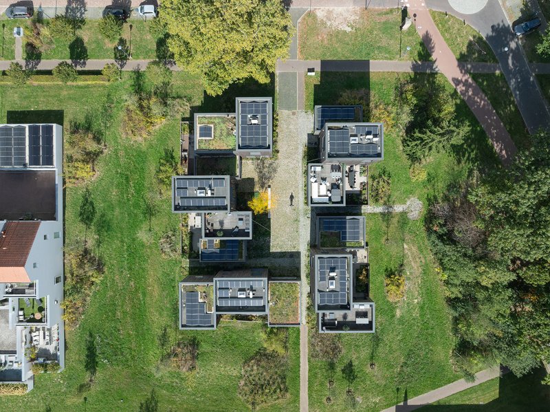 Aerial view of timber houses with photovoltaic panels arranged along a central pathway through green lots