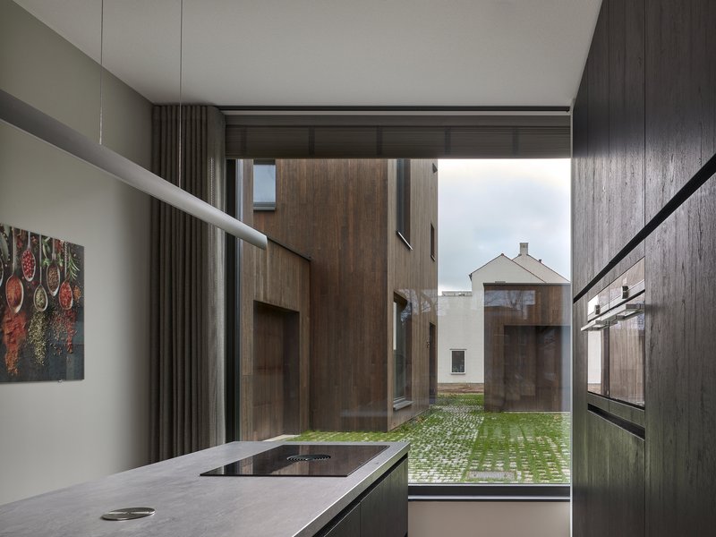 Kitchen window framing a view to timber-clad volumes across a courtyard with permeable paving