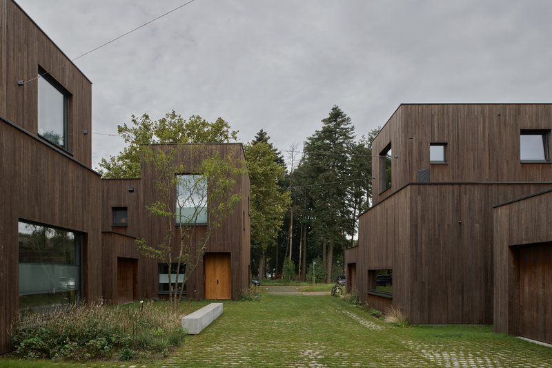 Shared courtyard with permeable paving between timber-clad dwellings under an overcast sky