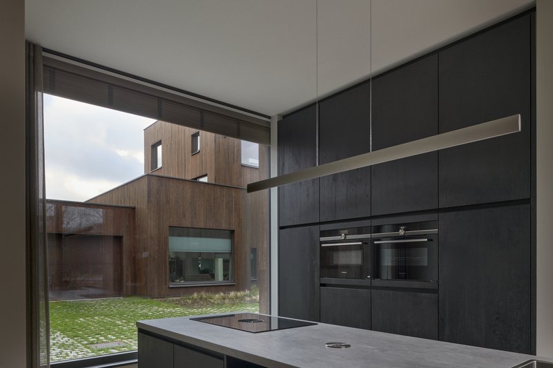 Kitchen with black cabinetry and island facing timber volumes through corner glazing