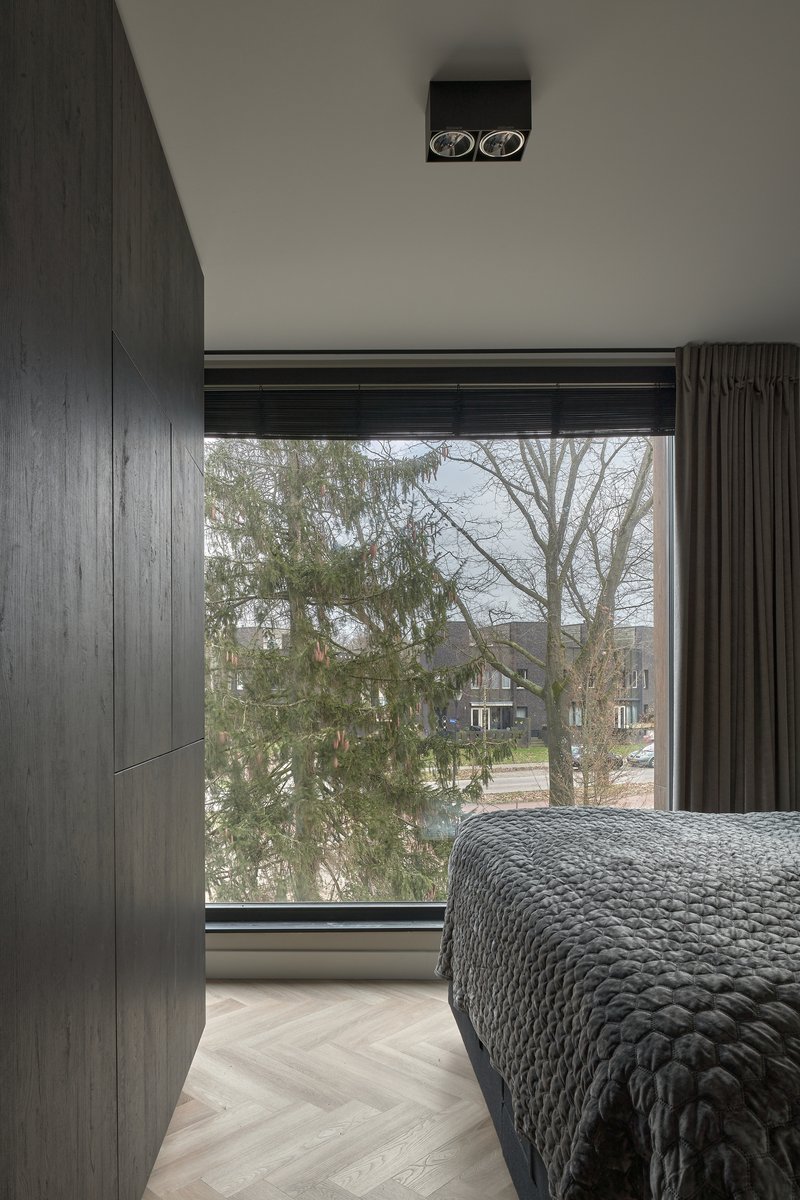 Bedroom with dark timber paneling and full-height window framing winter trees outside