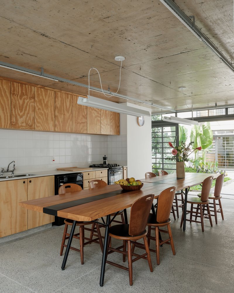Kitchen and dining area with plywood cabinetry, white tile backsplash, exposed concrete ceiling, and terrazzo flooring