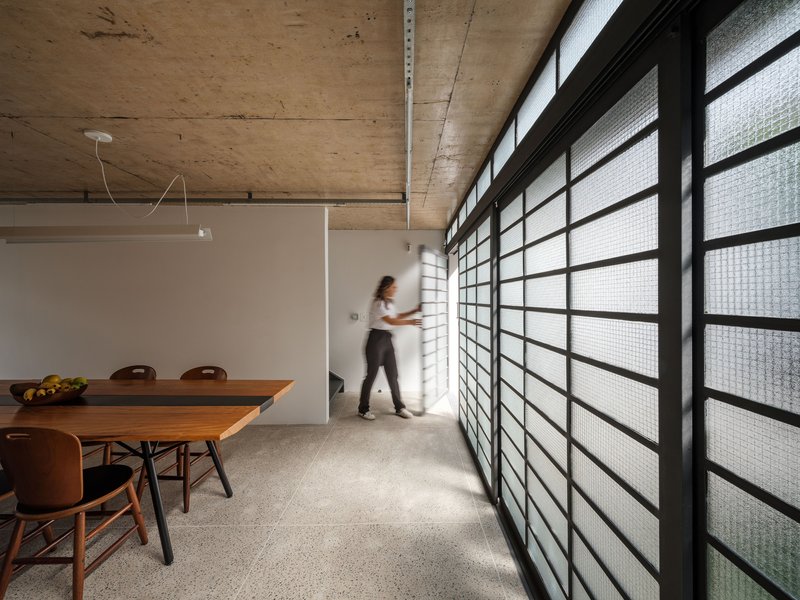 Interior with full-height glass block wall, figure walking in blurred motion, exposed concrete ceiling, and terrazzo floor