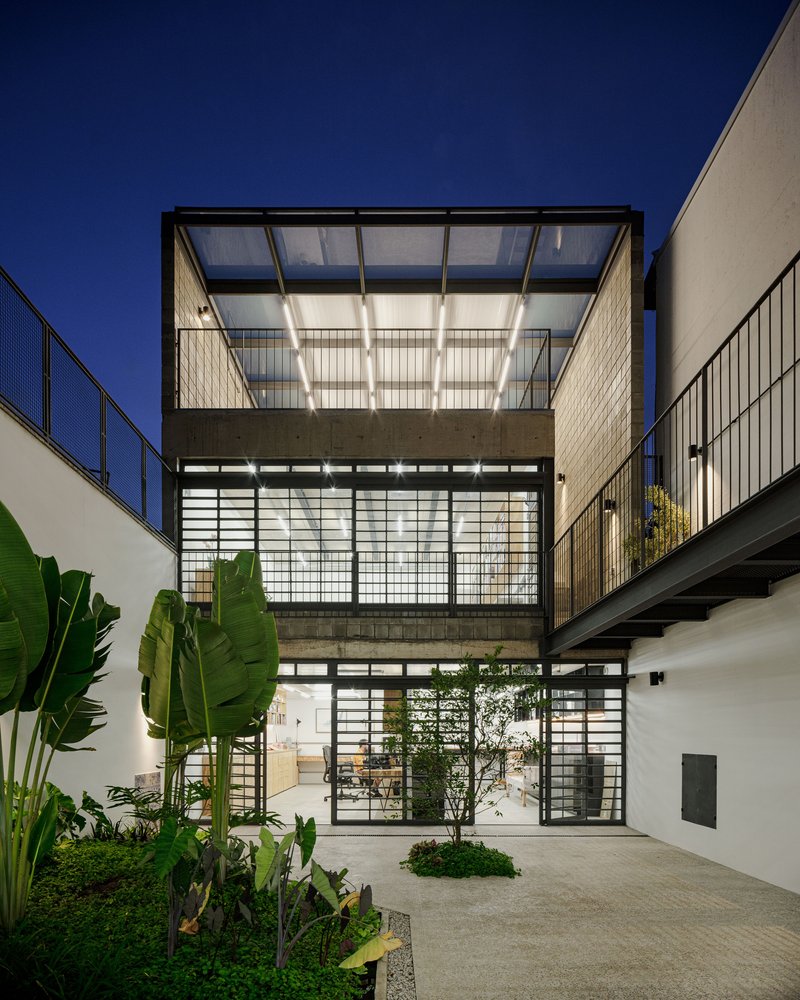 Three-story translucent glass and steel facade with planted courtyard at dusk