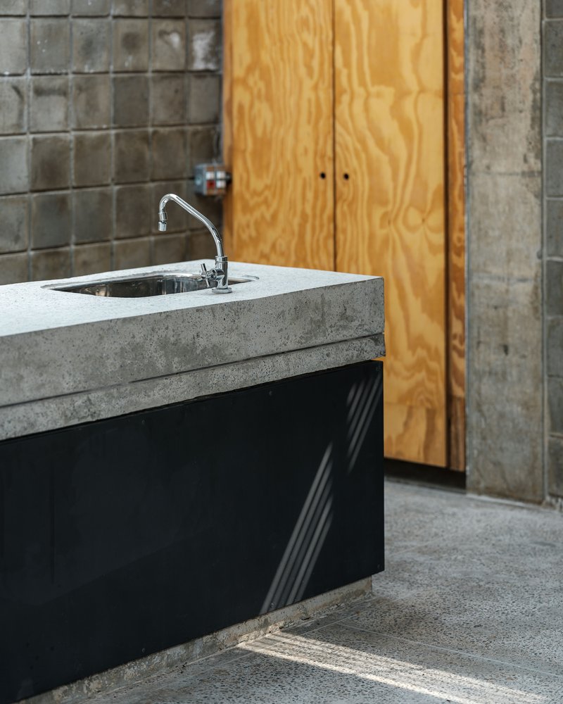 Concrete countertop with stainless steel sink against glazed tile wall and plywood cabinet doors