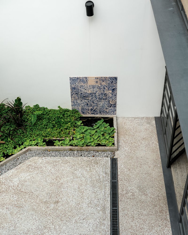 Top-down view of courtyard with planted bed, exposed aggregate paving, and patterned tile wall panel