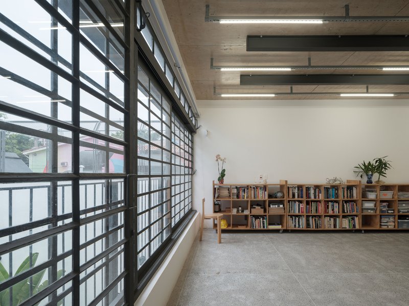 Interior reading room with gridded steel window wall, plywood ceiling with linear lighting, and low bookshelves