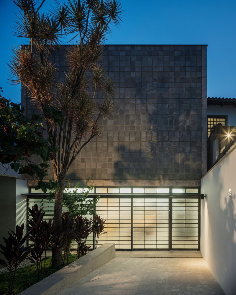 Tiled upper facade and translucent glass entry gate flanked by palm trees at twilight