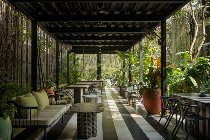 Covered terrace with black steel beam ceiling, green striped floor tiles, and layered vegetation on both sides
