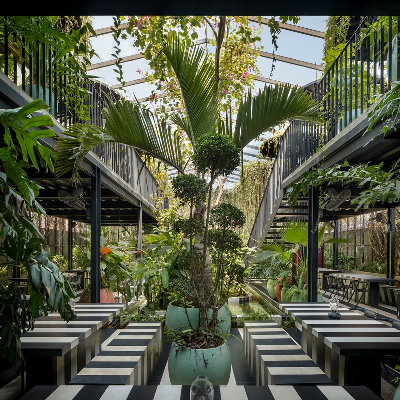 Central courtyard with striped concrete tables flanking potted trees under a glass and steel canopy
