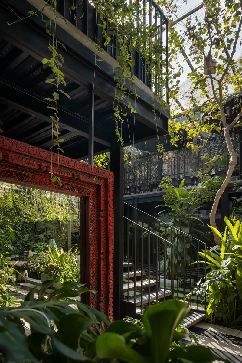 Carved red timber portal framing a courtyard garden beneath a steel-framed upper level with cascading vines