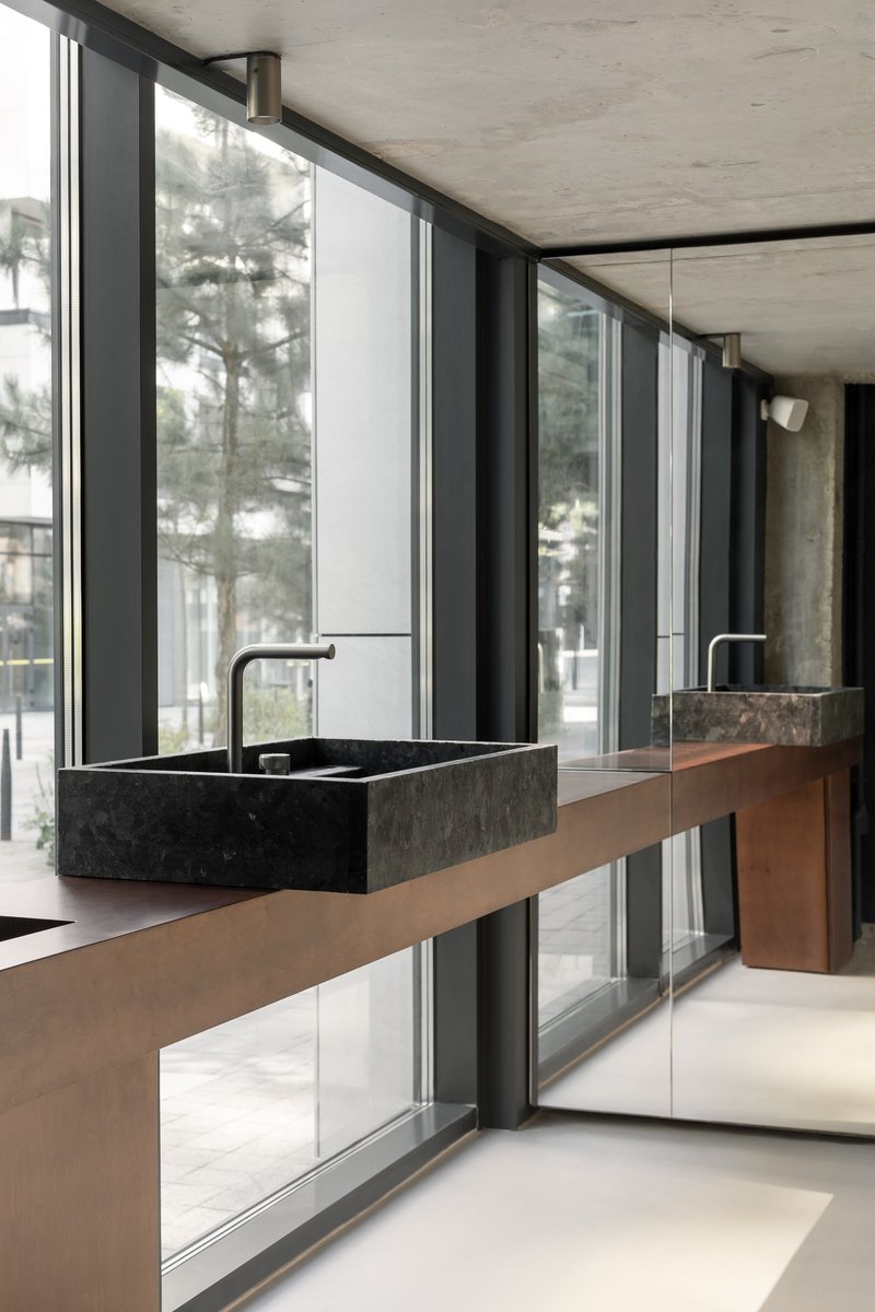 Cantilevered timber vanity with dark stone basin overlooking winter trees through floor-to-ceiling glazing