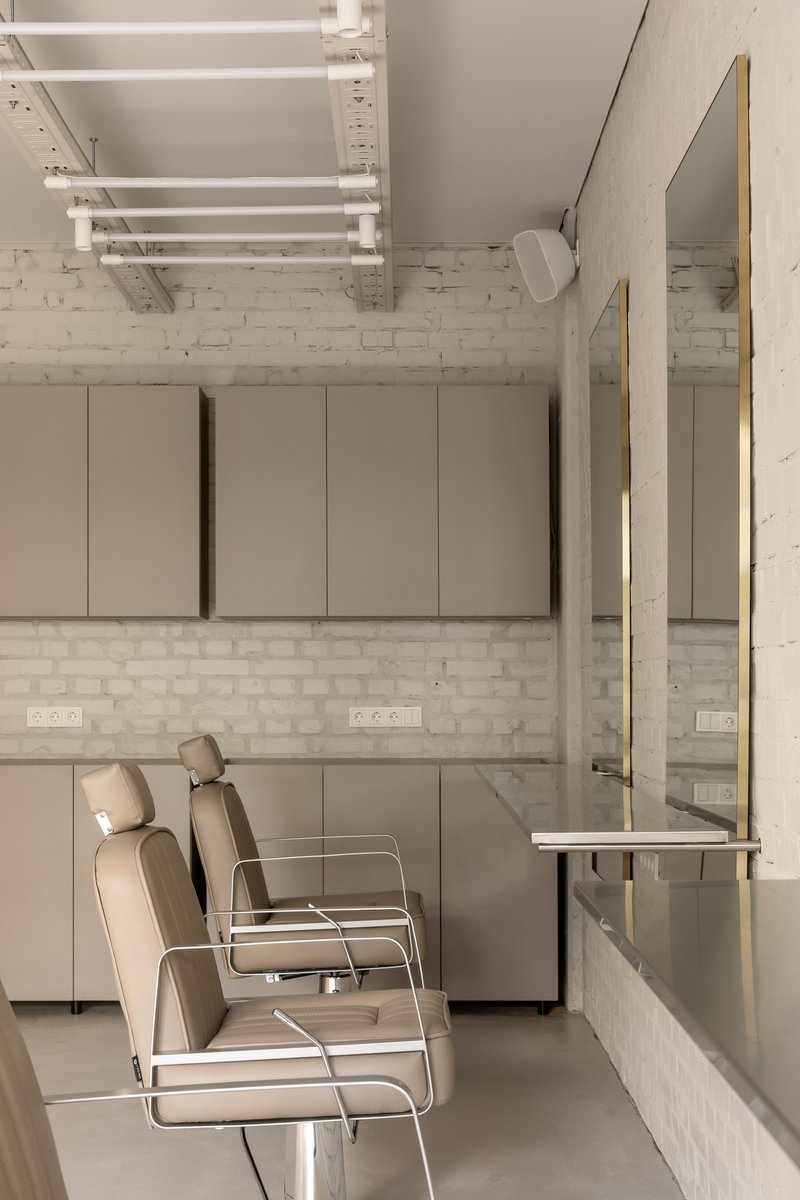 Salon chairs against white brick wall beneath exposed ceiling joists and wall-mounted cabinets