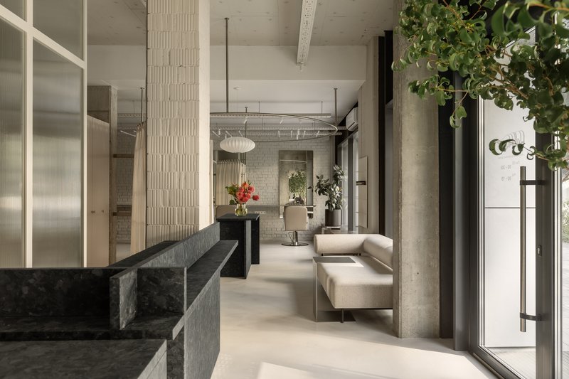 Open interior with dark stone reception counter, exposed concrete columns, and potted greenery near glazed entrance