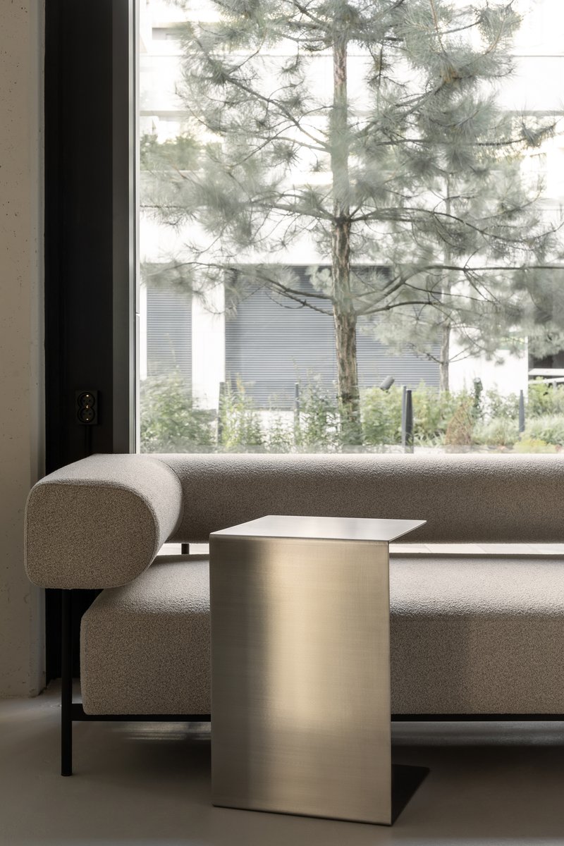 Grey upholstered sofa and brushed metal side table framed by a floor-to-ceiling window with pine tree outside